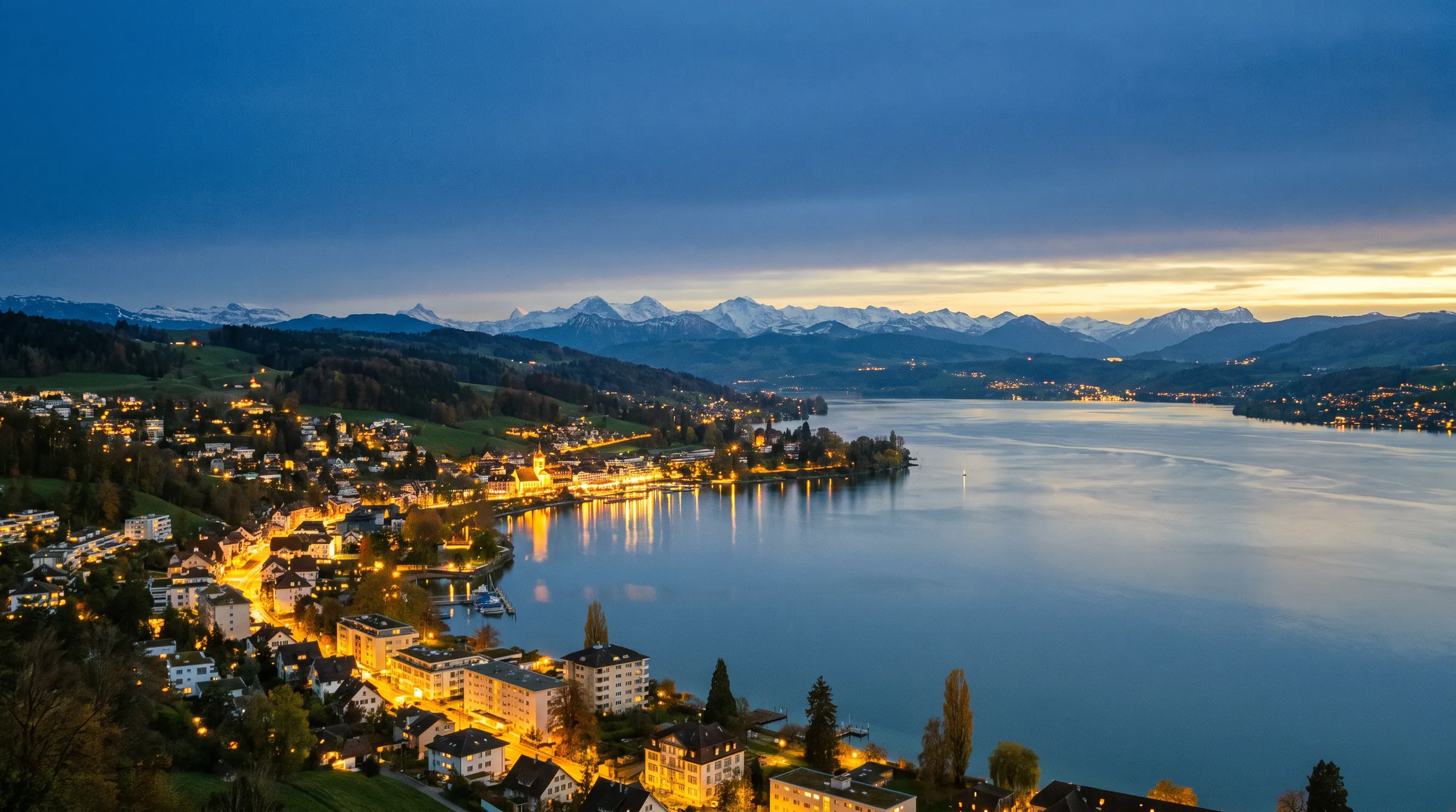 Evening over a Swiss lake with the lights of the lakeside towns and the Alps on the horizon